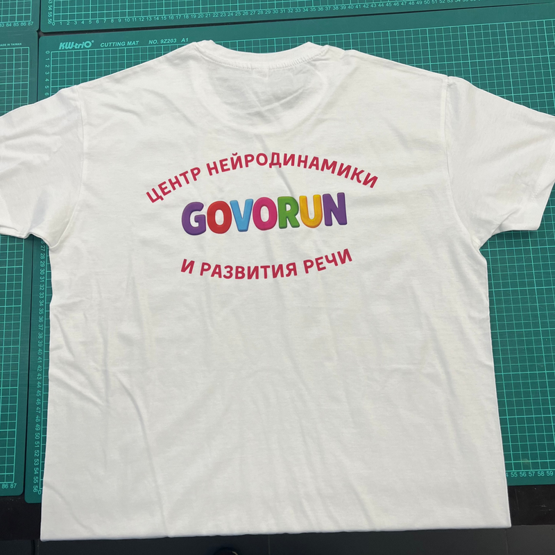 White t-shirt with colorful text on a green cutting mat