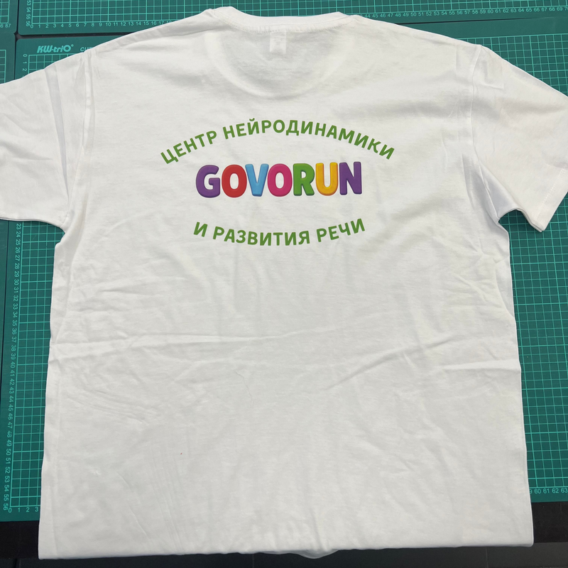 White t-shirt with colorful text on a green cutting mat